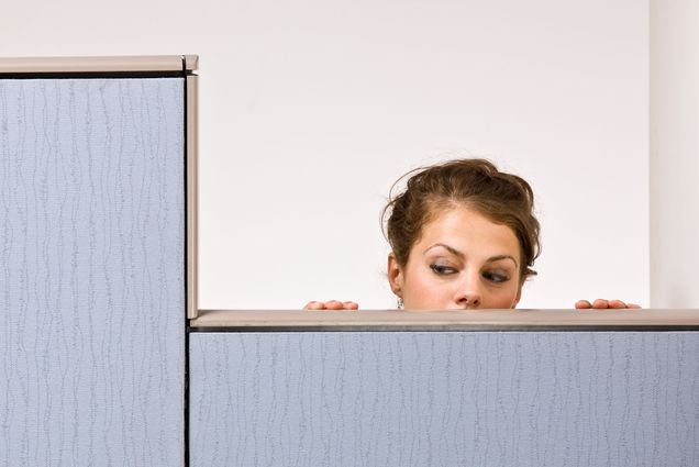 Photo: A businesswoman peering over cubicle wall