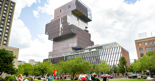 Photo: Boston University's COM Lawn filled with students on a sunny day. The Center for Computing and Data Sciences on Boston University's campus is visible in the background