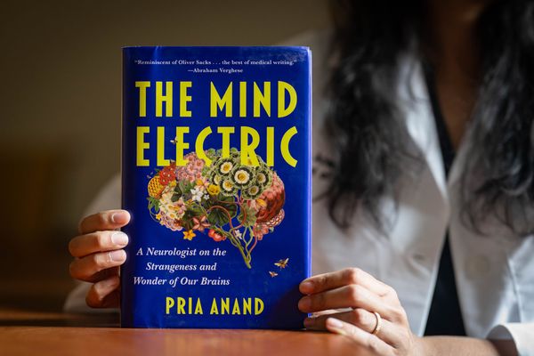 Photo: Pria Anand holding up her book "The Mind Electric," which features a vibrant blue cover and an illustration of the brain with flowers making up different parts