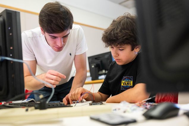 Photo: A young college students helps a younger middle school student on an engineering project.
