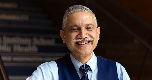 Photo: A man wearing a blue dress shirt and a navy blue vest with a tie leans on a stairwell and smiles for a portrait shot.