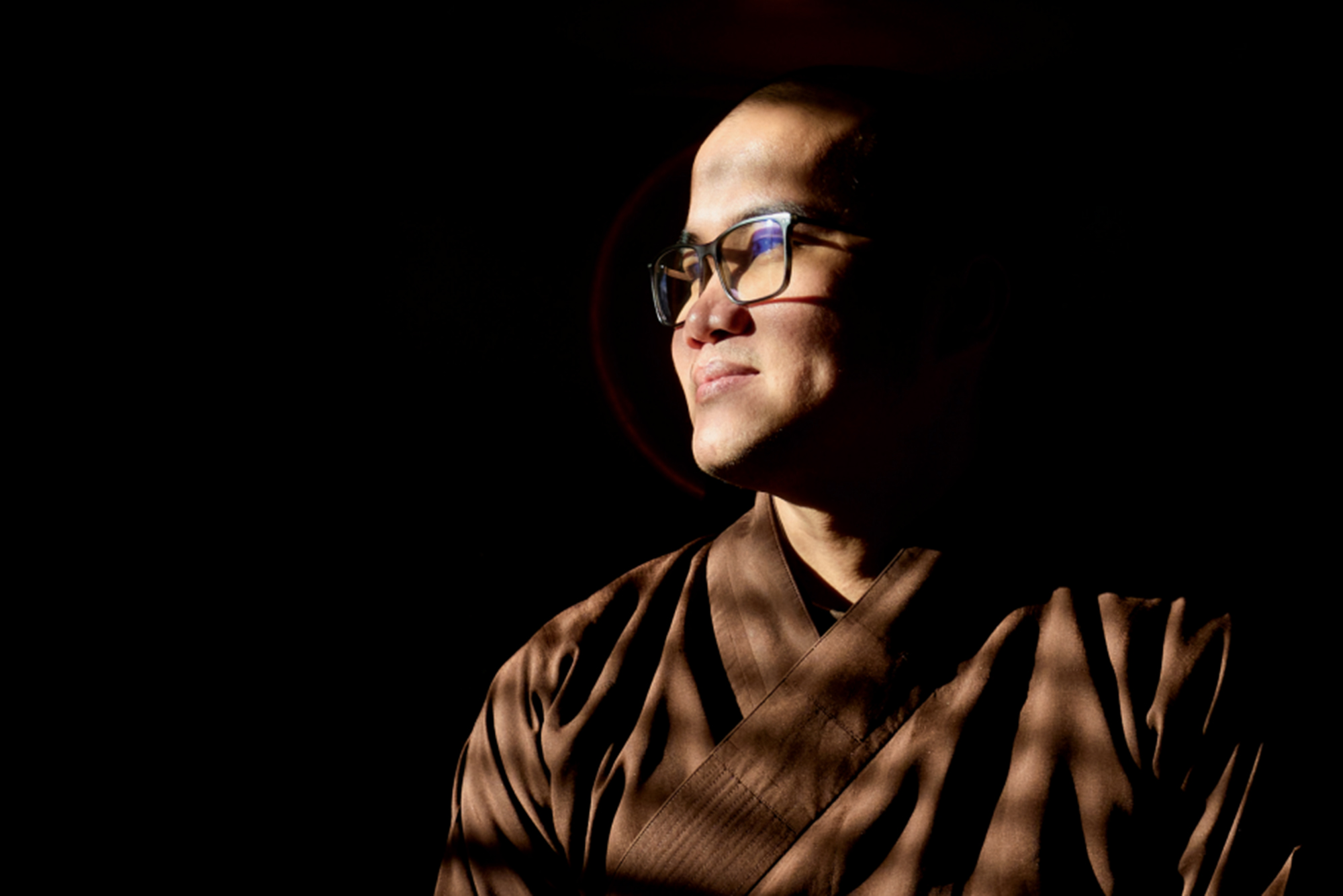 Photo: A person wearing glasses and staring off into the distance in front of a dark background