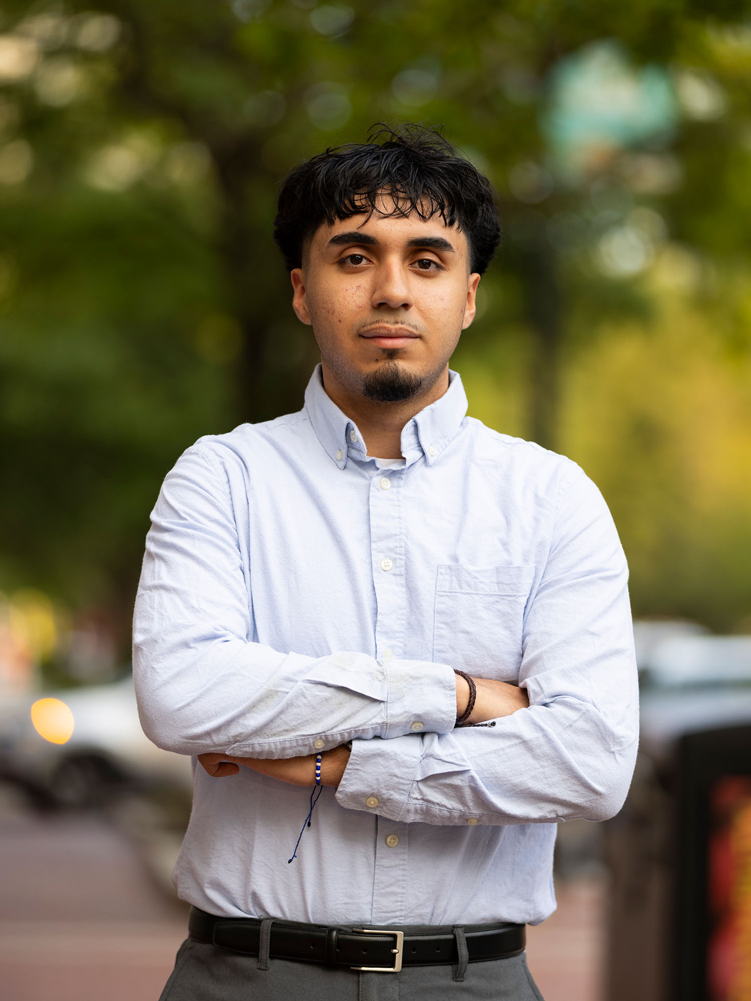 Photo: Julio Perez, a BU student in a light, long-sleeved button down shirt posing with his arms crossed outdoors