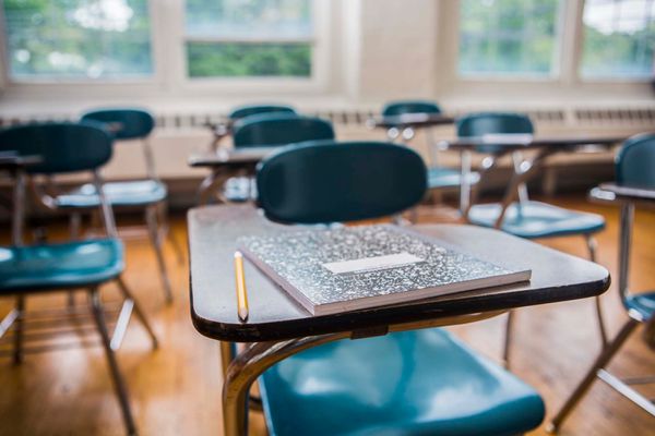 Photo: A stock image of a notebook and pencil on a desk in a school classroom