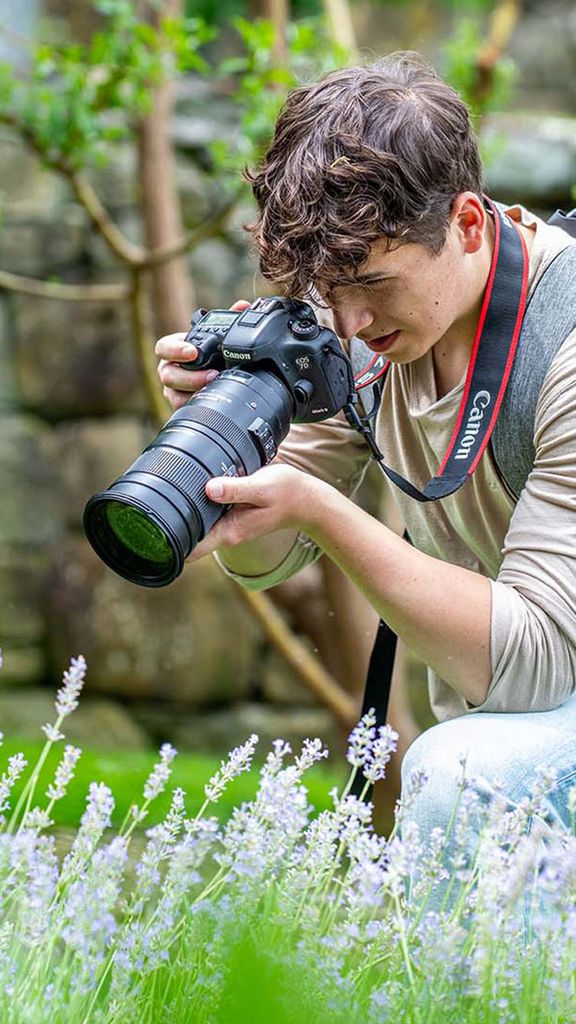 Photo: A person taking a photo, with a professional camera, of flowers in a field