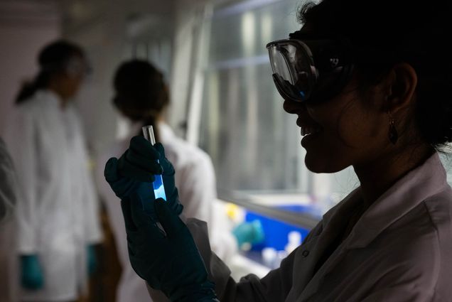 Photo: A shadowed shot of an individual holding a vial of liquid in a lab.