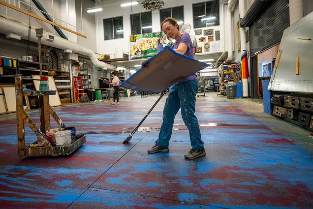 Photo: A person holding a flat piece of cardboard while painting a floor length piece.