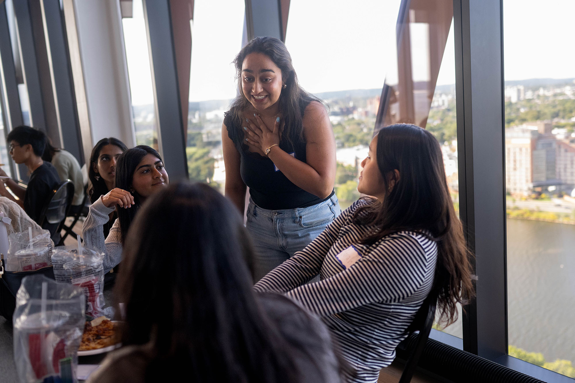 Photo: A woman smiling with her hand on her chest as she talks to a group of people sitting down