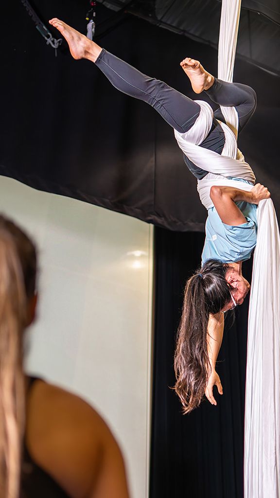 Photo: A woman in athletic clothing is wrapped up in a hanging fabric, performing aerial acrobatics.