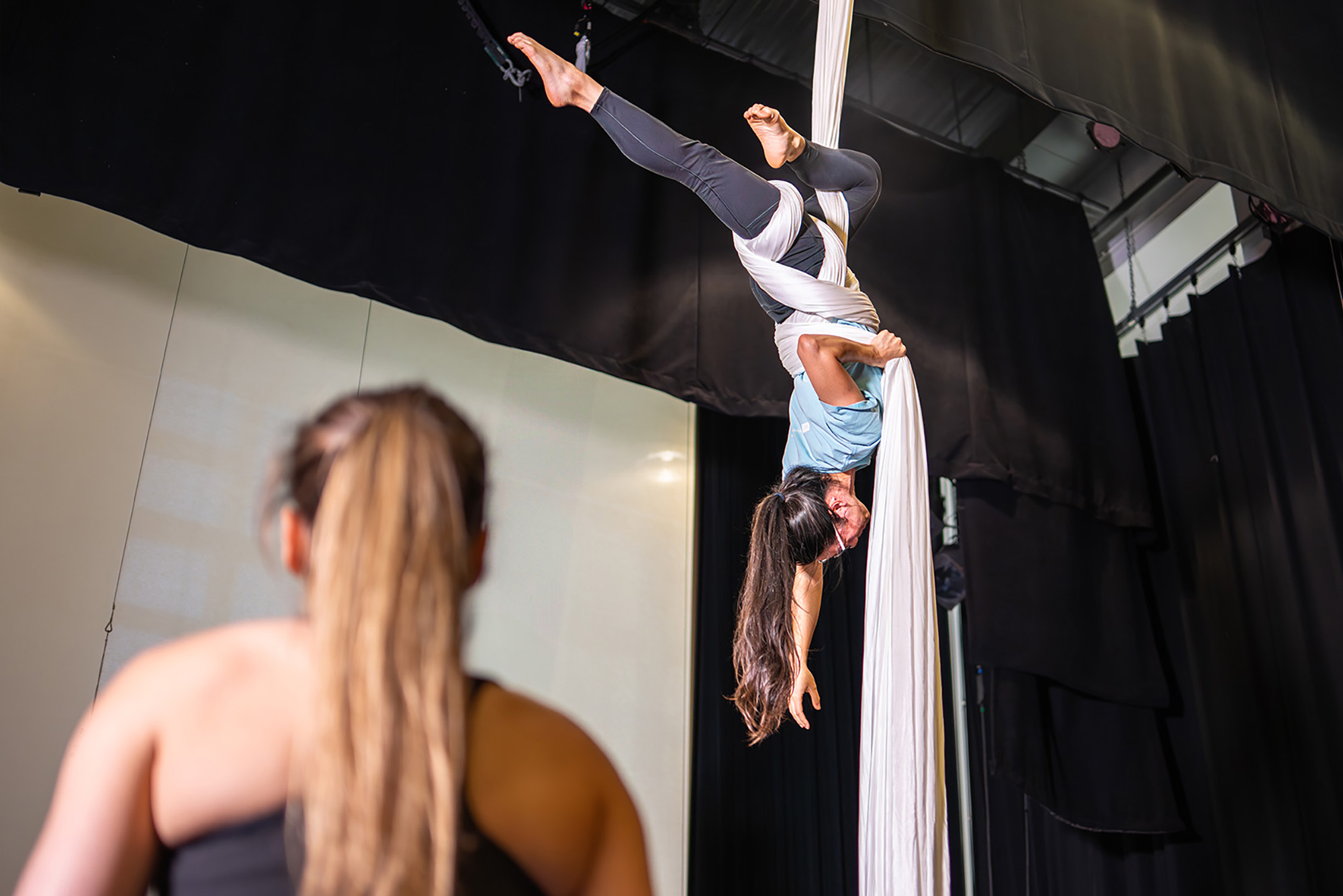 Photo: A woman in athletic clothing is wrapped up in a hanging fabric, performing aerial acrobatics.