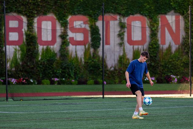 Photo: A college student kicks a soccerball under a large red sign reading "Boston"