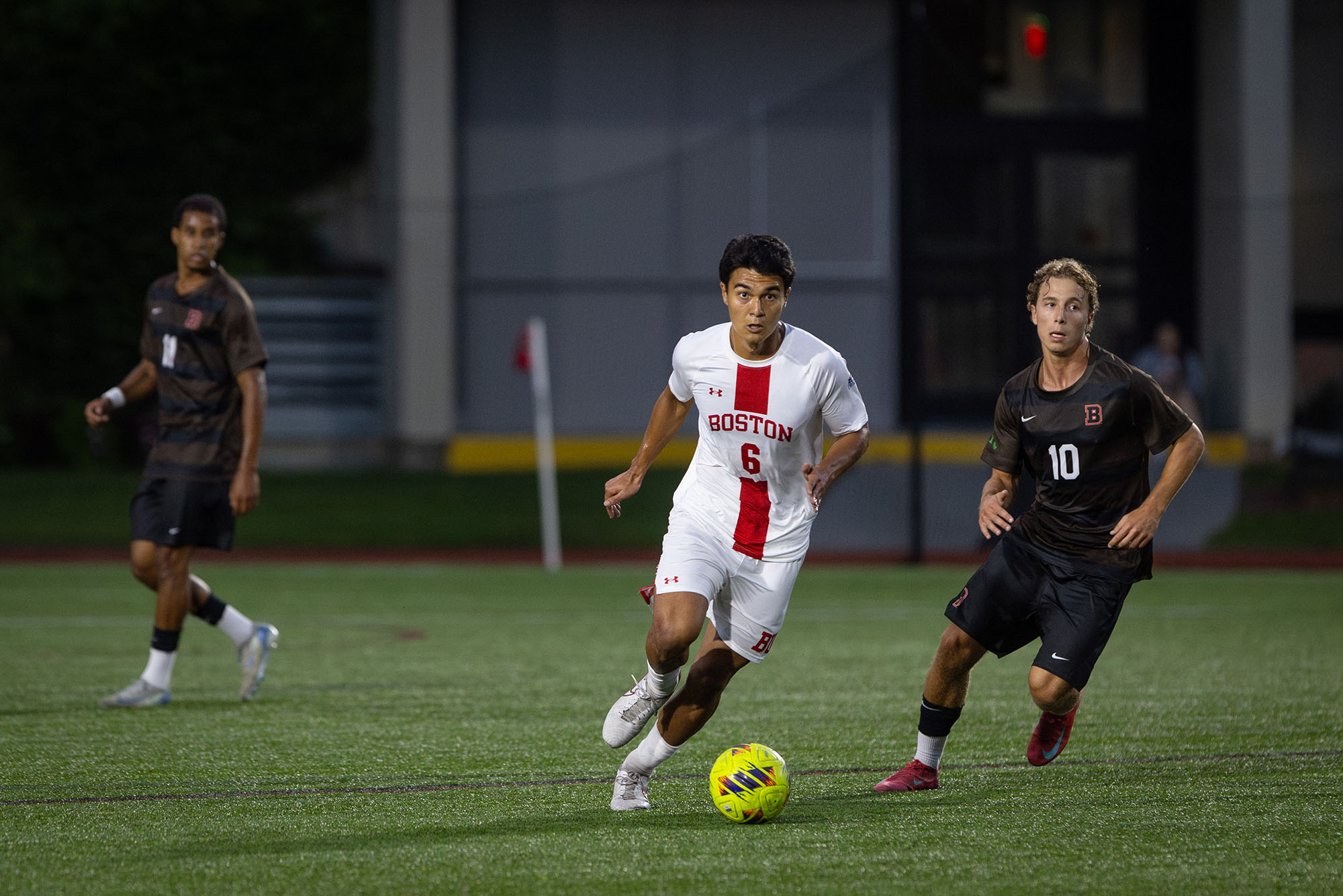Photo: A BU Men's soccer player in a white uniform with red trim kicking the ball down the field
