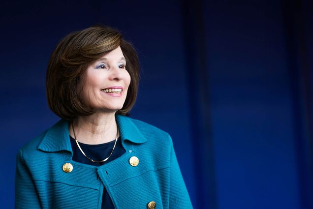 Photo: A portrait of Gloria Waters, a white woman with short brown hair wearing a blue jacket against a darker blue background.