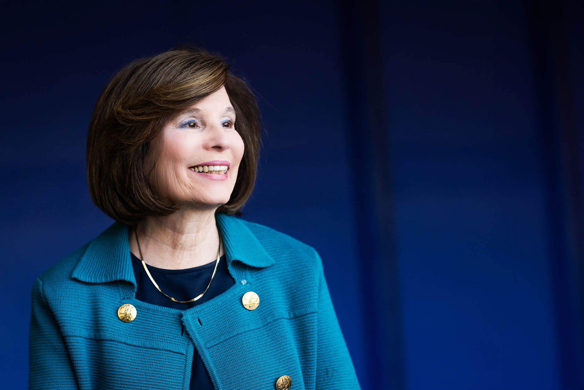 Photo: A portrait of Gloria Waters, a white woman with short brown hair wearing a blue jacket against a darker blue background.