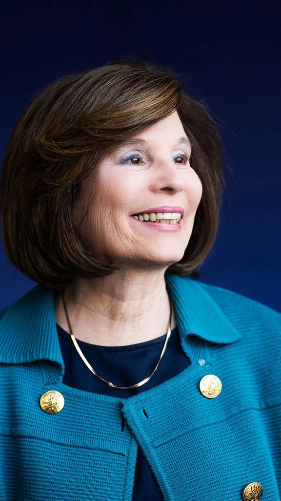 Photo: A portrait of Gloria Waters, a white woman with short brown hair wearing a blue jacket against a darker blue background.