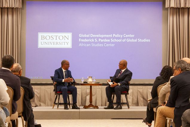 Photo: Two people sitting on stage during an event in front of a crowd