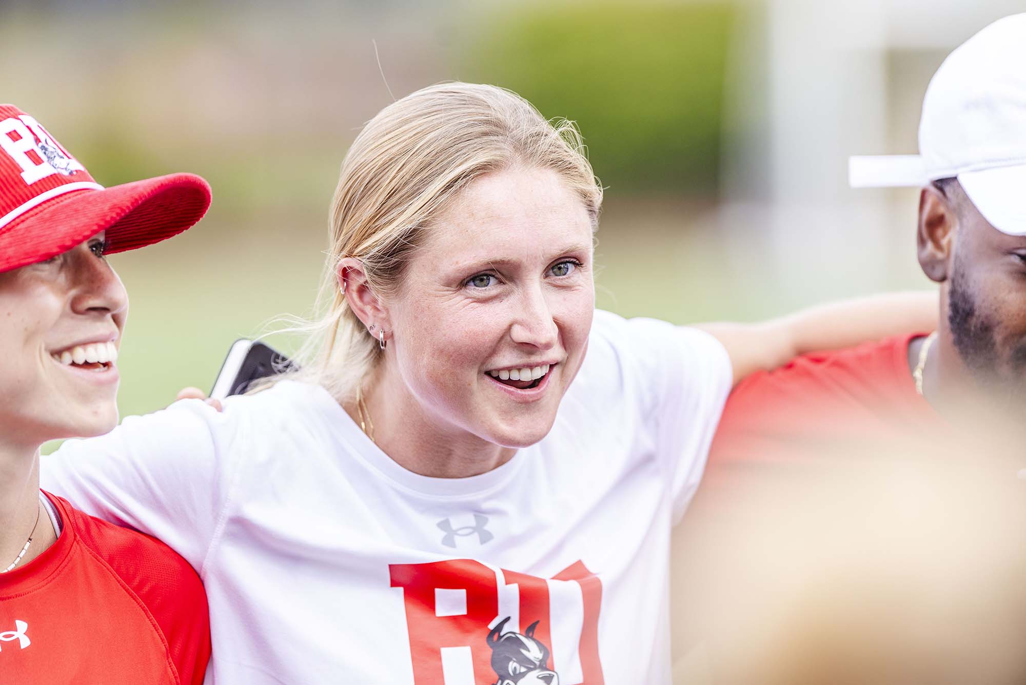 Photo: A white woman with blonde hair relaxes against her coaches with her arms thrown around their shoulders.
