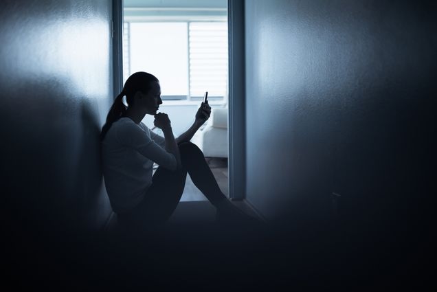 Photo: A woman sits on the floor of a dark room looking at her phone
