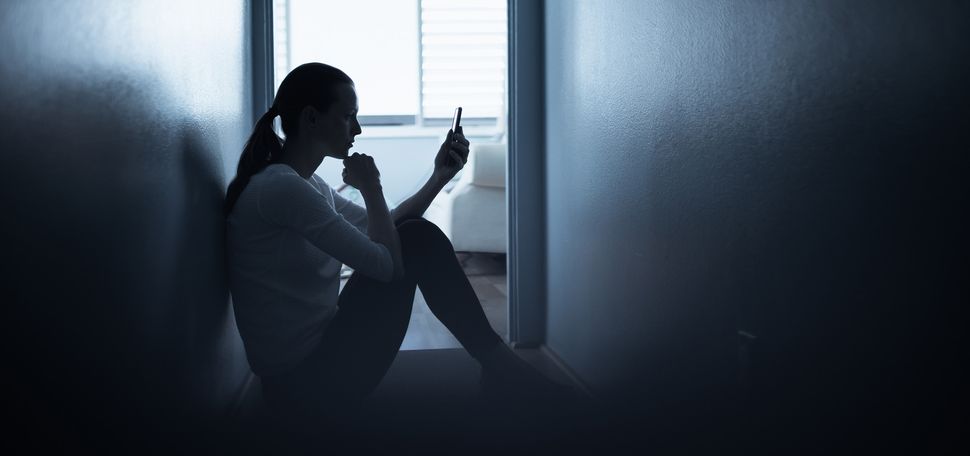 Photo: A woman sits on the floor of a dark room looking at her phone