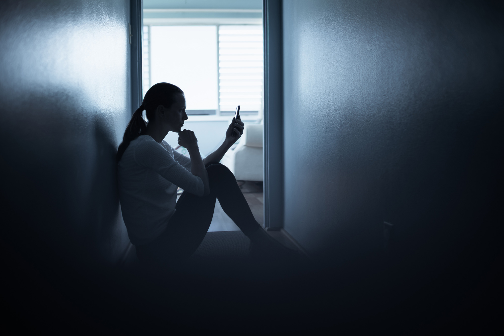 Photo: A woman sits on the floor of a dark room looking at her phone