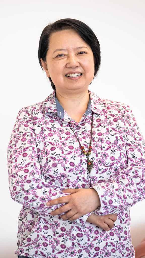 Photo: An Asian woman with short hair posing for a headshot in front of a white wall