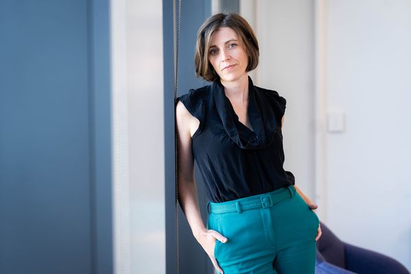 Photo: A woman with short hair leans against a blue wall in this posed formal portrait