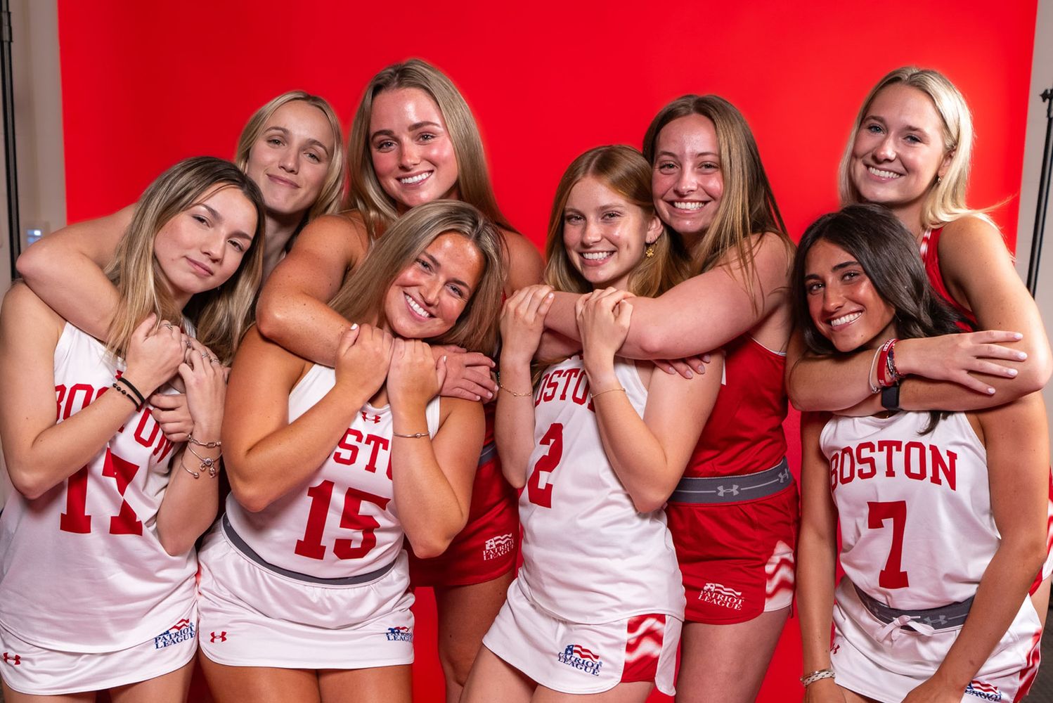 Photo: Four sets of sisters on the BU field hockey team smiling and hugging in uniform in front of a red background