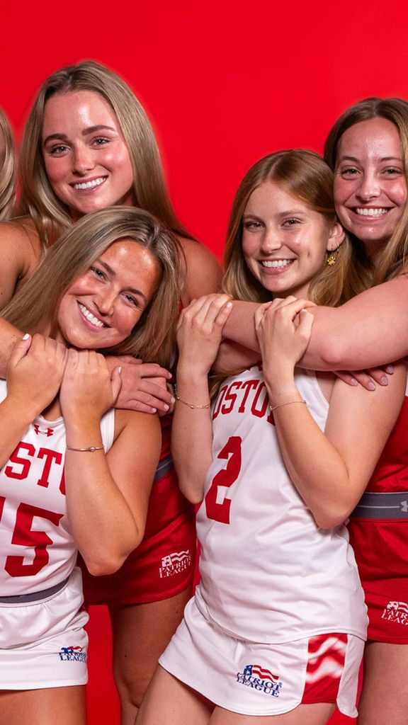 Photo: Four sets of sisters on the BU field hockey team smiling and hugging in uniform in front of a red background