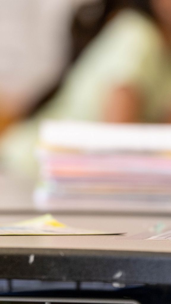 Photo: A close-up of an elementary student writing with a pencil with school supplies on their desk