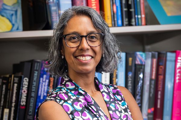 Photo: A portrait of a woman with chin length gray hair wearing a purple and blue sleeveless blouse. She smiles for the photo