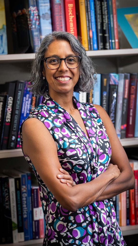 Photo: A portrait of a woman with chin length gray hair wearing a purple and blue sleeveless blouse. She smiles for the photo