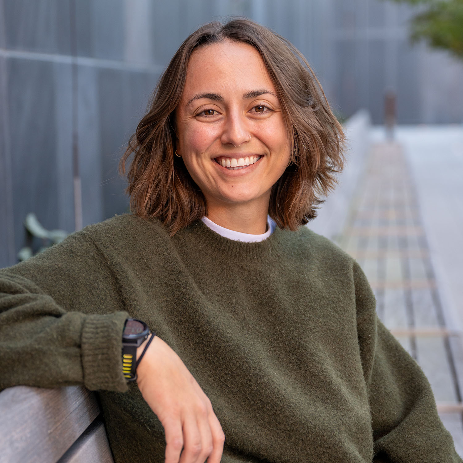Photo: A photo of Marybeth Surratt, a woman with short brown hair, smiling as she sits on a bench outside