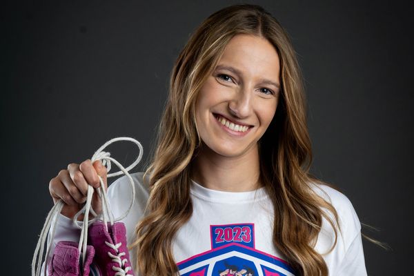 Photo: Hannah Bryson, a female wrestler at BU, holding up purple wrestling shoes and posing with a smile