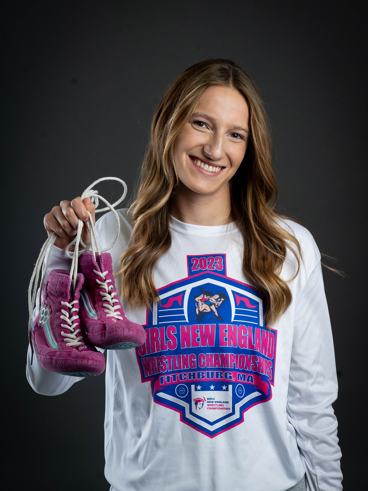 Photo: Hannah Bryson, a female wrestler at BU, holding up purple wrestling shoes and posing with a smile