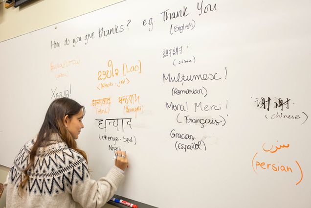 Photo: A woman writing on a whiteboard that says "How do you give thanks?" with many different ways to say "Thank You" in other languages