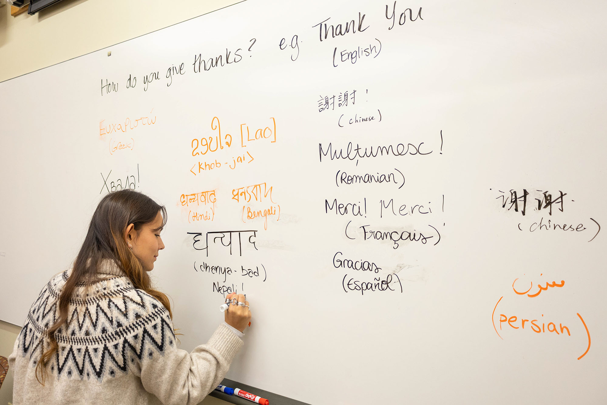 Photo: A woman writing on a whiteboard that says "How do you give thanks?" with many different ways to say "Thank You" in other languages