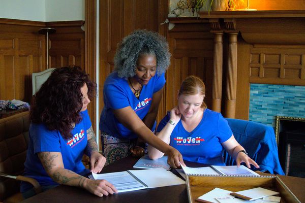 Photo: Three women from WoVeN wearing blue tshirts and looking at paperwork