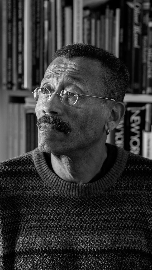 Photo: A black and white photo of production designer Wynn Thomas in front of a bookshelf