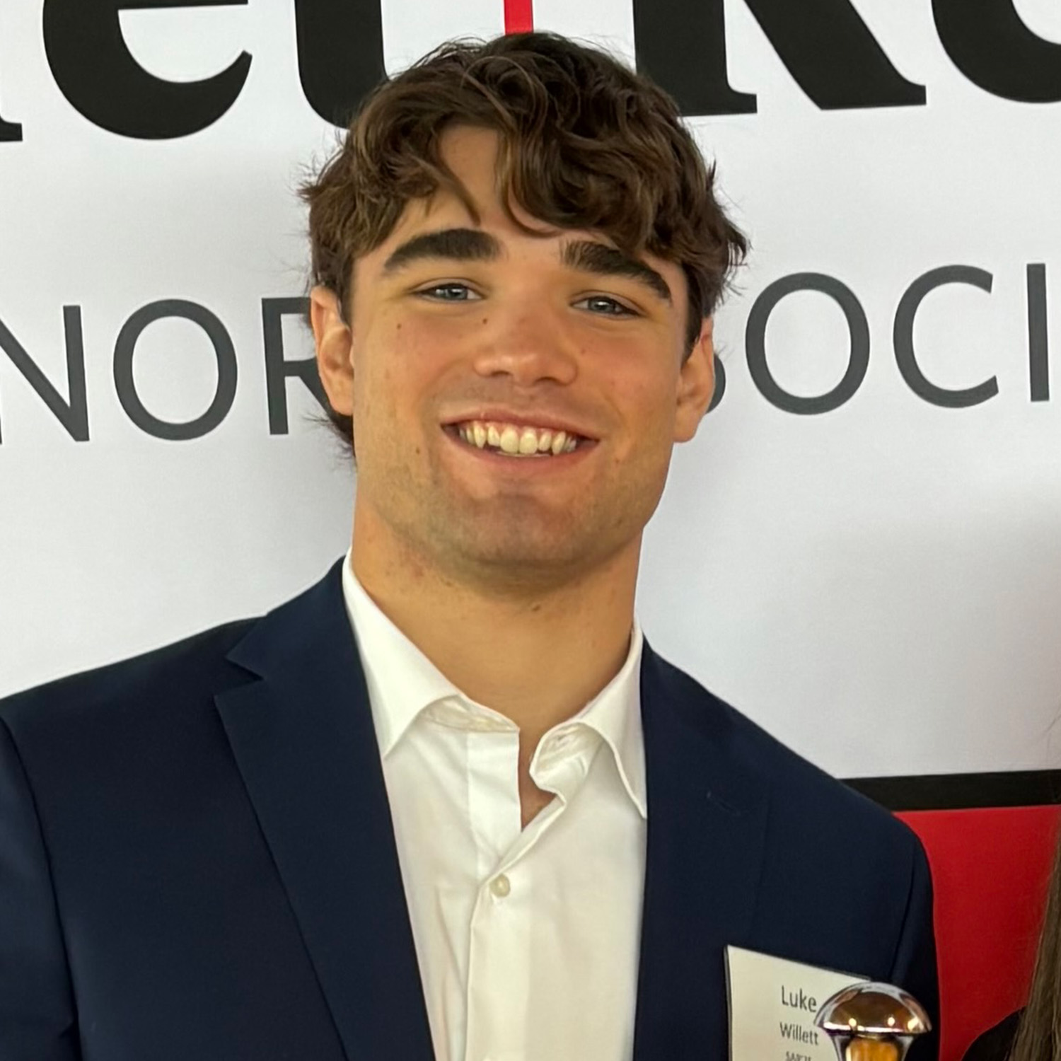 Photo: Luke Willett, a man with brown hair, smiling and wearing a suit during an event