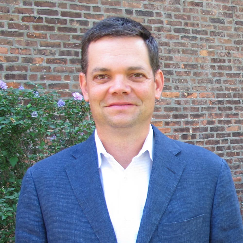 Photo: A portrait shot of a white man wearing a blue suit and white button up.