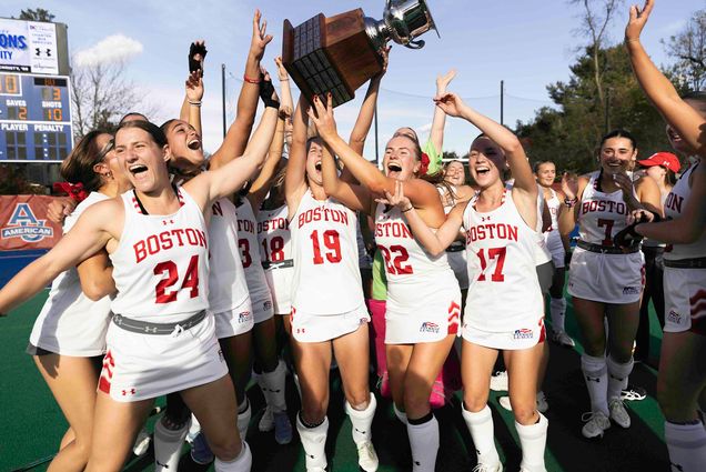 Photo: BU's field hockey team celebrate a Patriot League win, holding the trophy while wearing their white uniform.