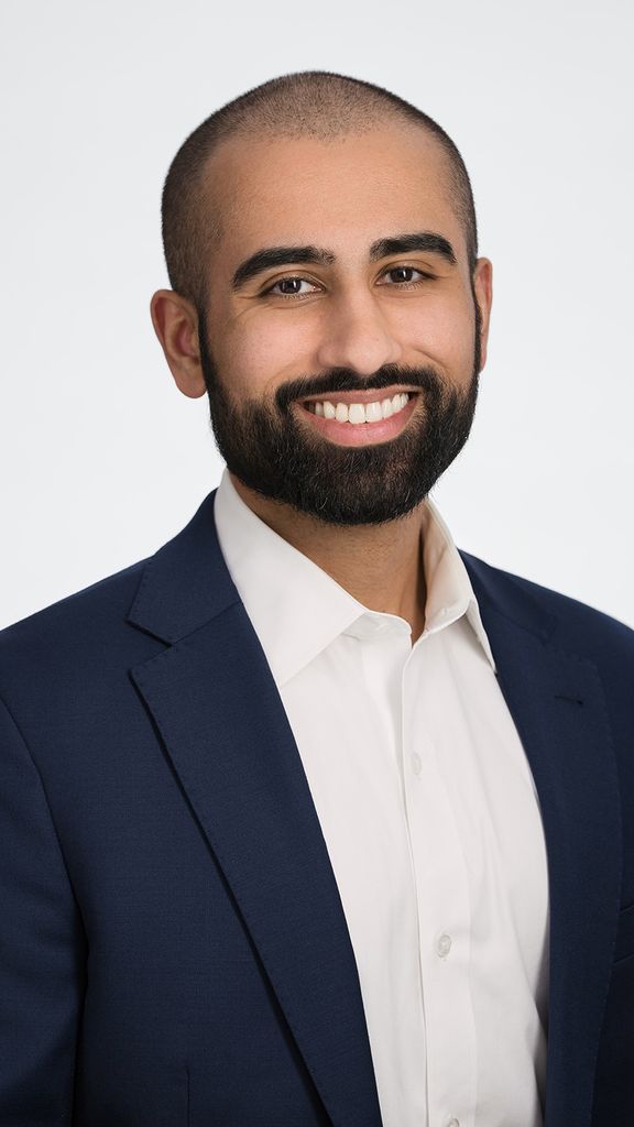 Photo: A headshot of a man in a suti smiling in front of a white background