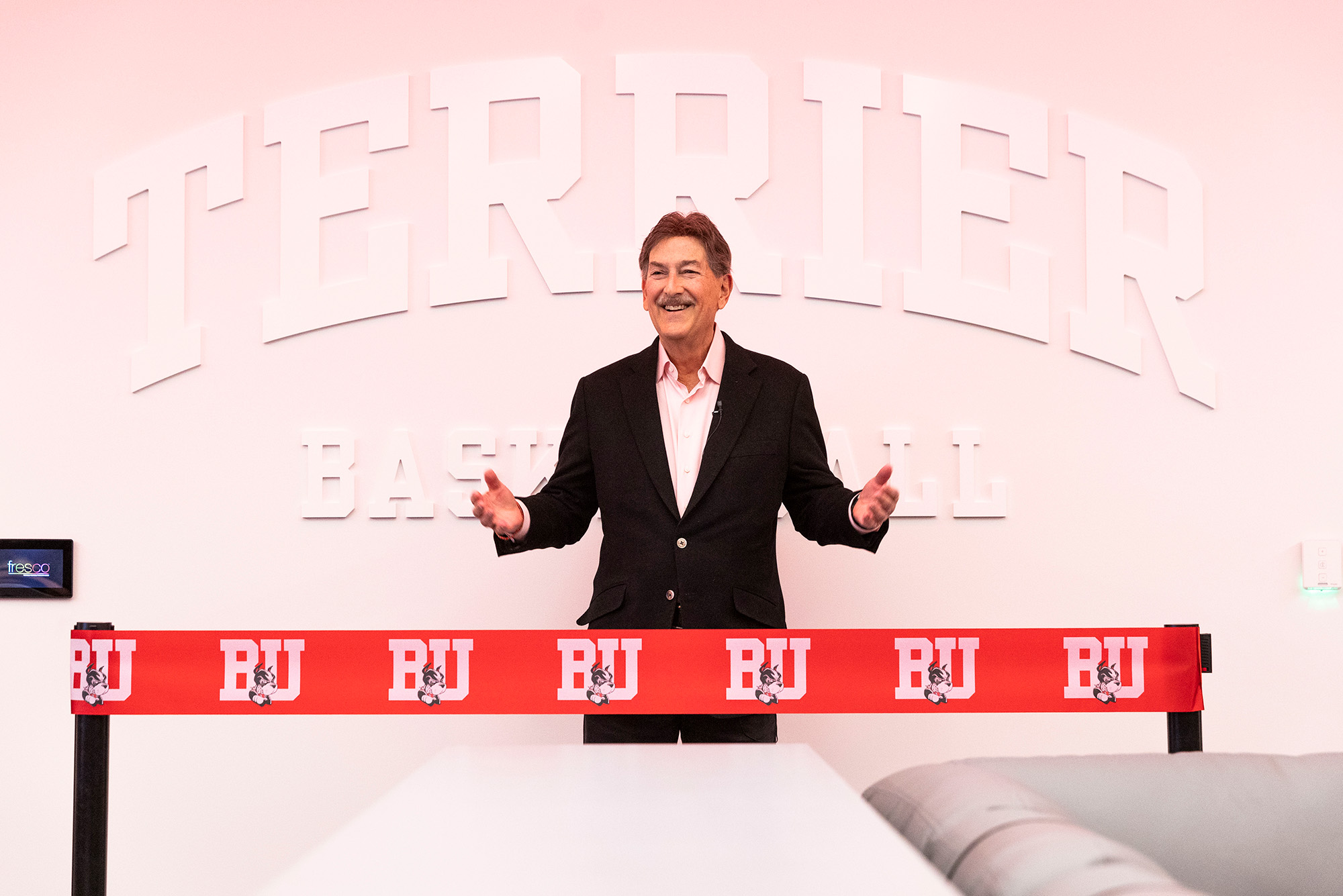 Photo: Ike Brown, a white man in a suit, stands behind a red ribbon for a locker room revealing.