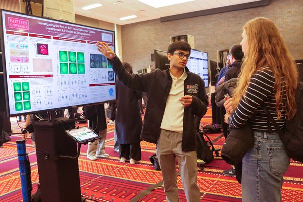 Photo: A male BU student standing in front of a board presenting their research. The board reads "Investigating the Role of Bcl11b on Embryonic Cardiac Development & Function in Xenopus laevis"
