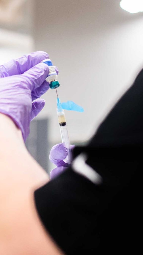 Photo: A stock image of a clinician fills a syringe with a vaccine to administer to a student