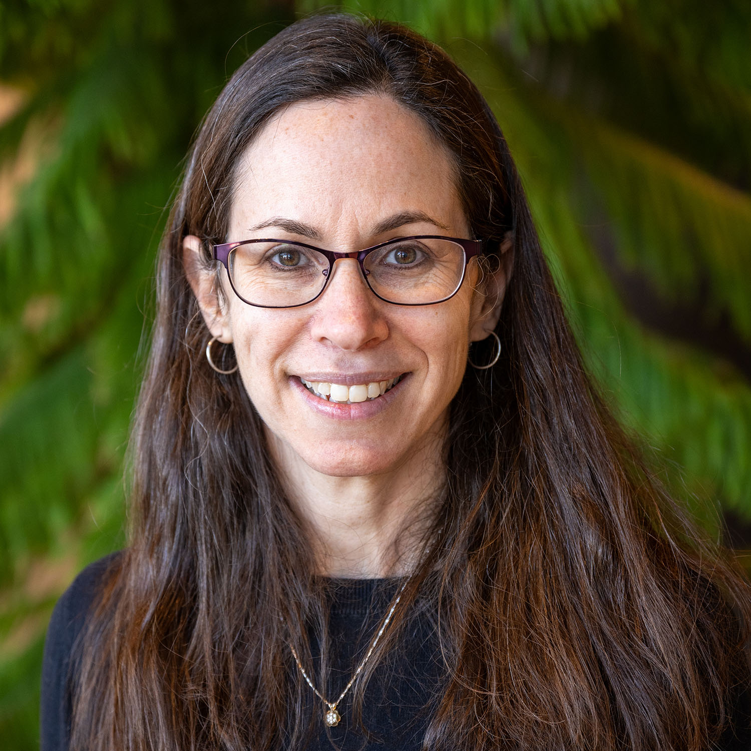 Photo: Pamela Templer, a distinguished professor and chair of biology at Boston University, posing in front of foliage for a headshot. She is smiling and wearing brown-rimmed glasses