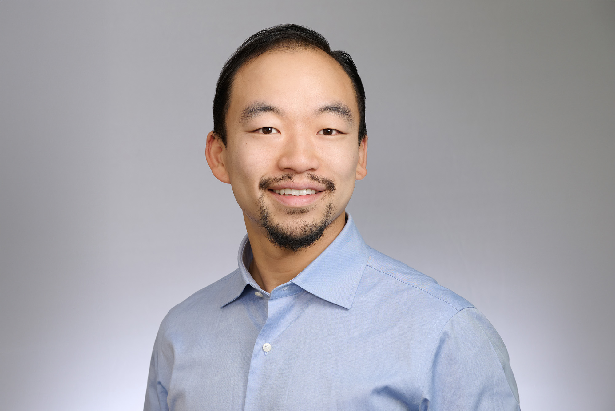 Photo: Michael Chang, assistant professor of language and literacy education at Wheelock College of Education & Human Development, smiling and posing in a blue shirt with a gray background