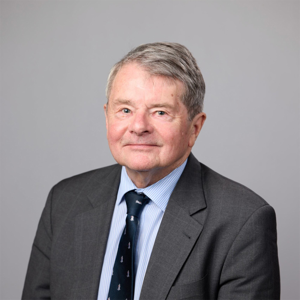 Photo: A white man with short gray hair in a gray suit jacket and a blue button up poses for a portrait image