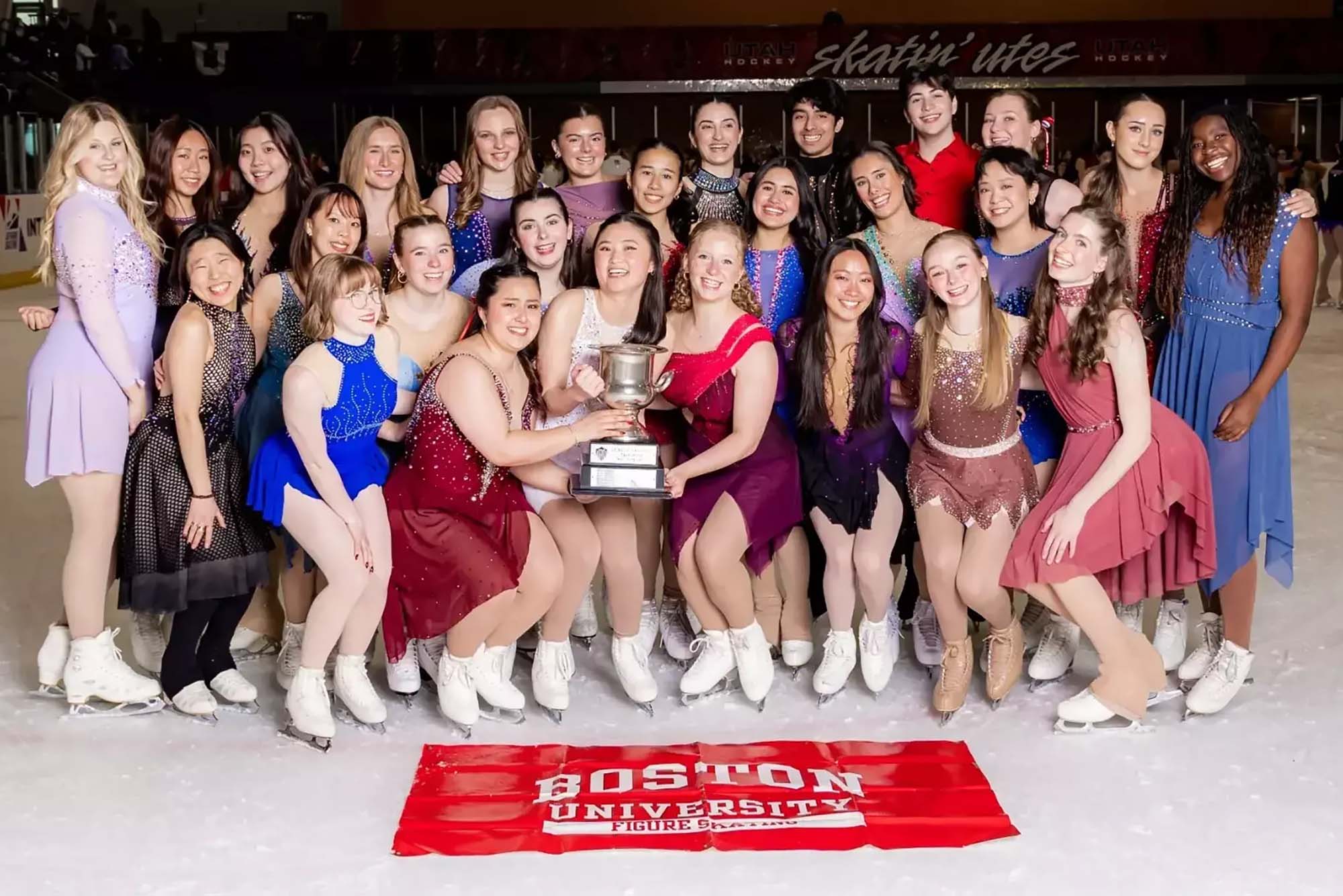 Photo: A group shot of figure skating team with a trophy on the ice with the BOSTON UNIVERSITY banner in front of them