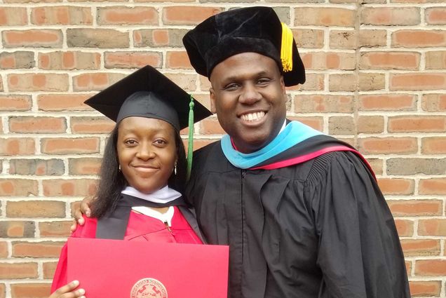 Photo: Two individuals stand next to each other, a graduate and a professor, both in graduation regalia